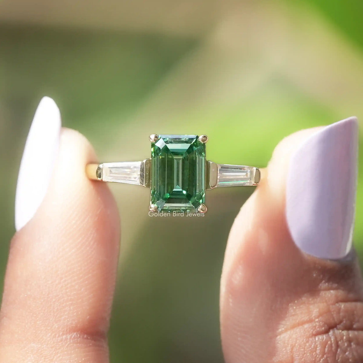 Two fingers holding the Green Emerald Cut Moissanite Engagement Ring 