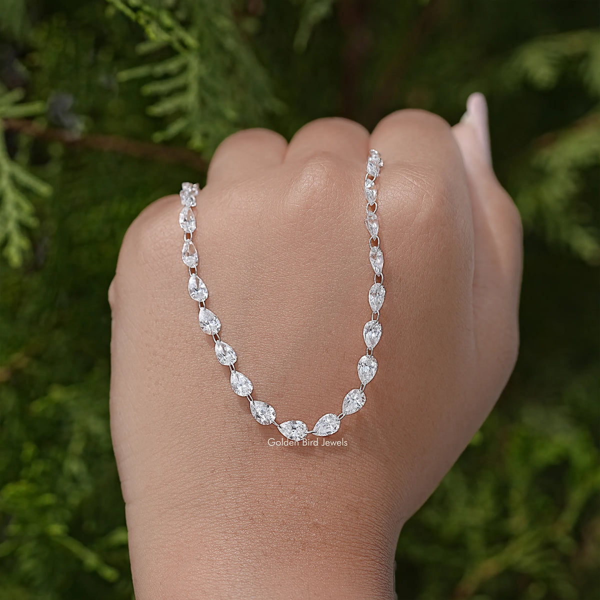 Silver pear-cut diamond tennis necklace held in hand, teardrop stations