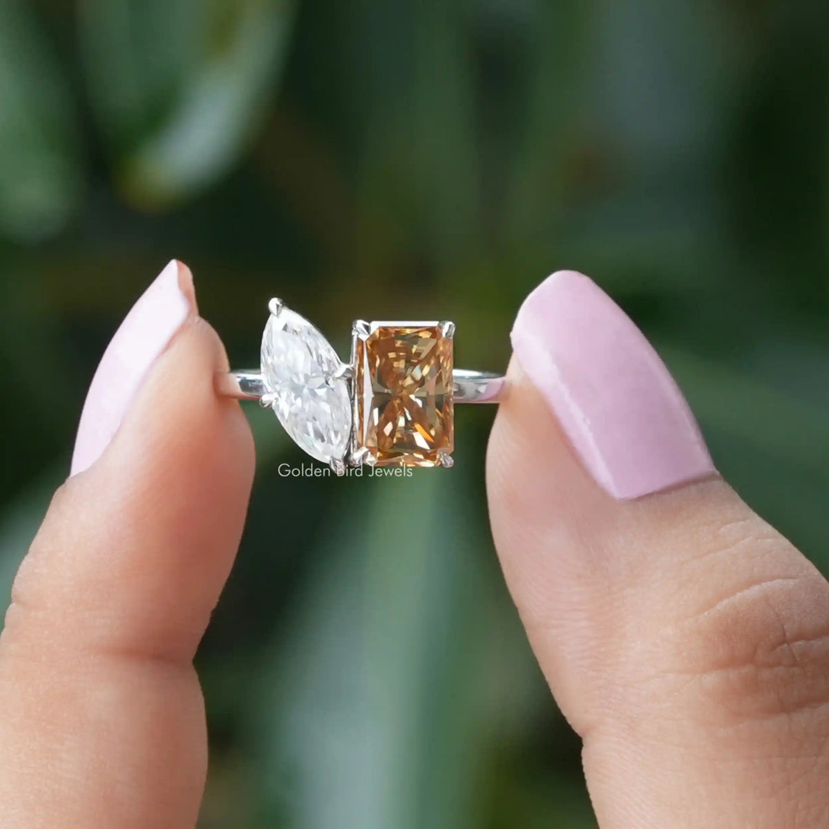 Two fingers holding the Champagne Radiant Cut Toi Et Moi Ring