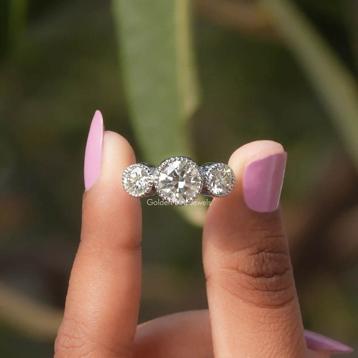 Two fingers holding the Bezel Set Round Cut Moissanite Ring