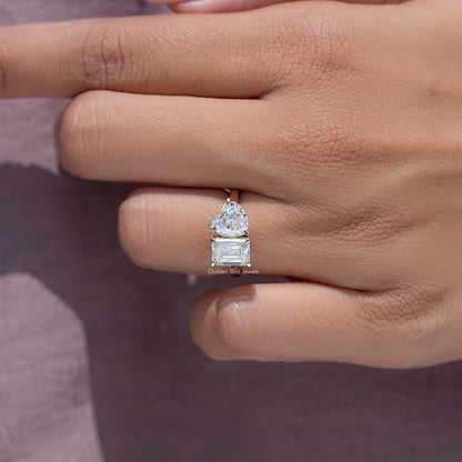 Toi et moi ring on finger, featuring emerald-cut and heart-shaped moissanite stones.