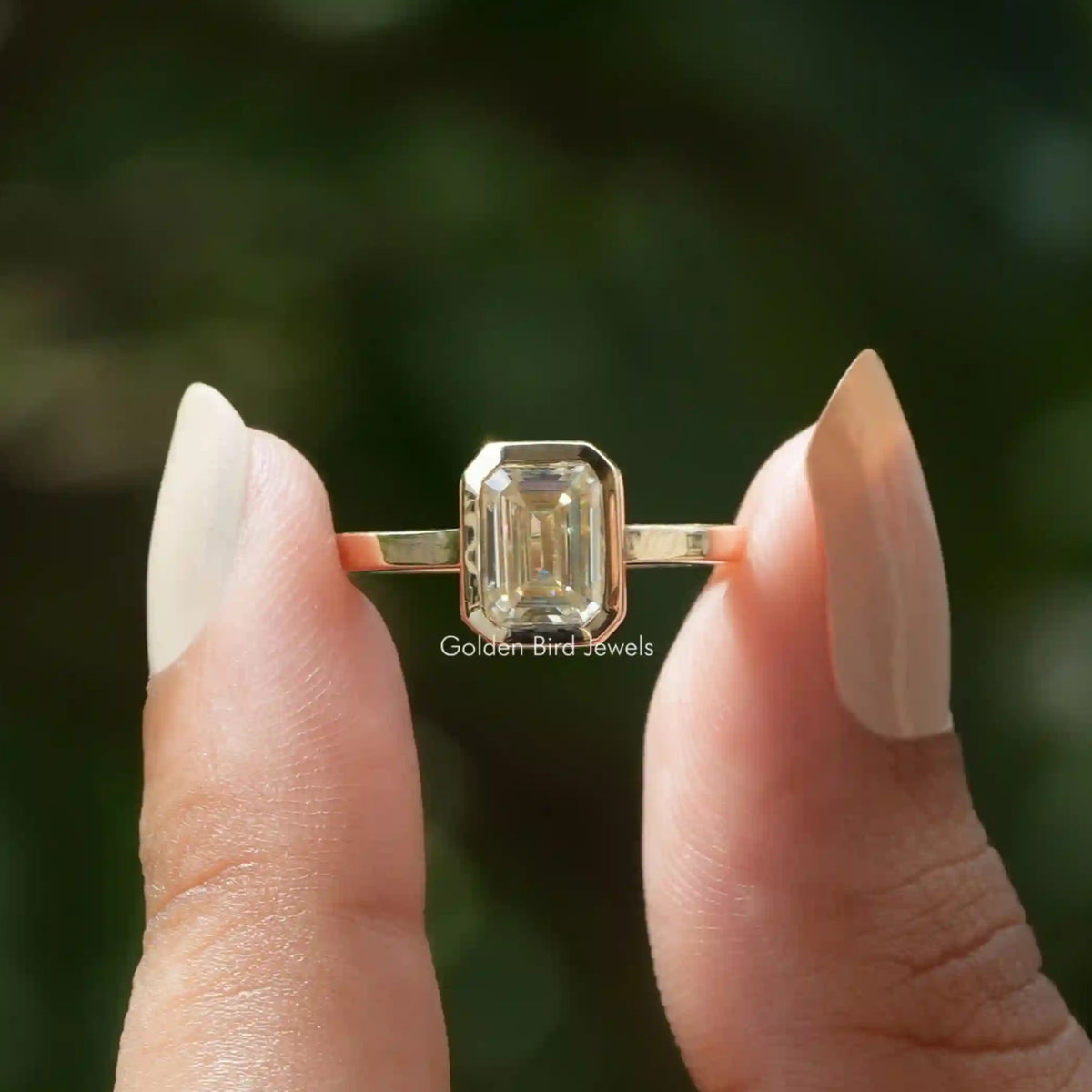 Two fingers holding emerald cut solitaire moissanite ring.