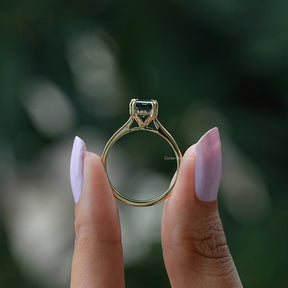 Back view of emerald cut moissanite   ring in holding two fingers 

