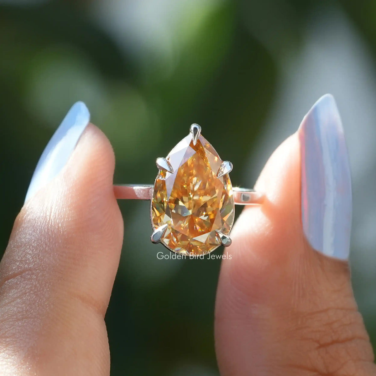 Two fingers holding the Moissanite pear cut solitaire wedding ring