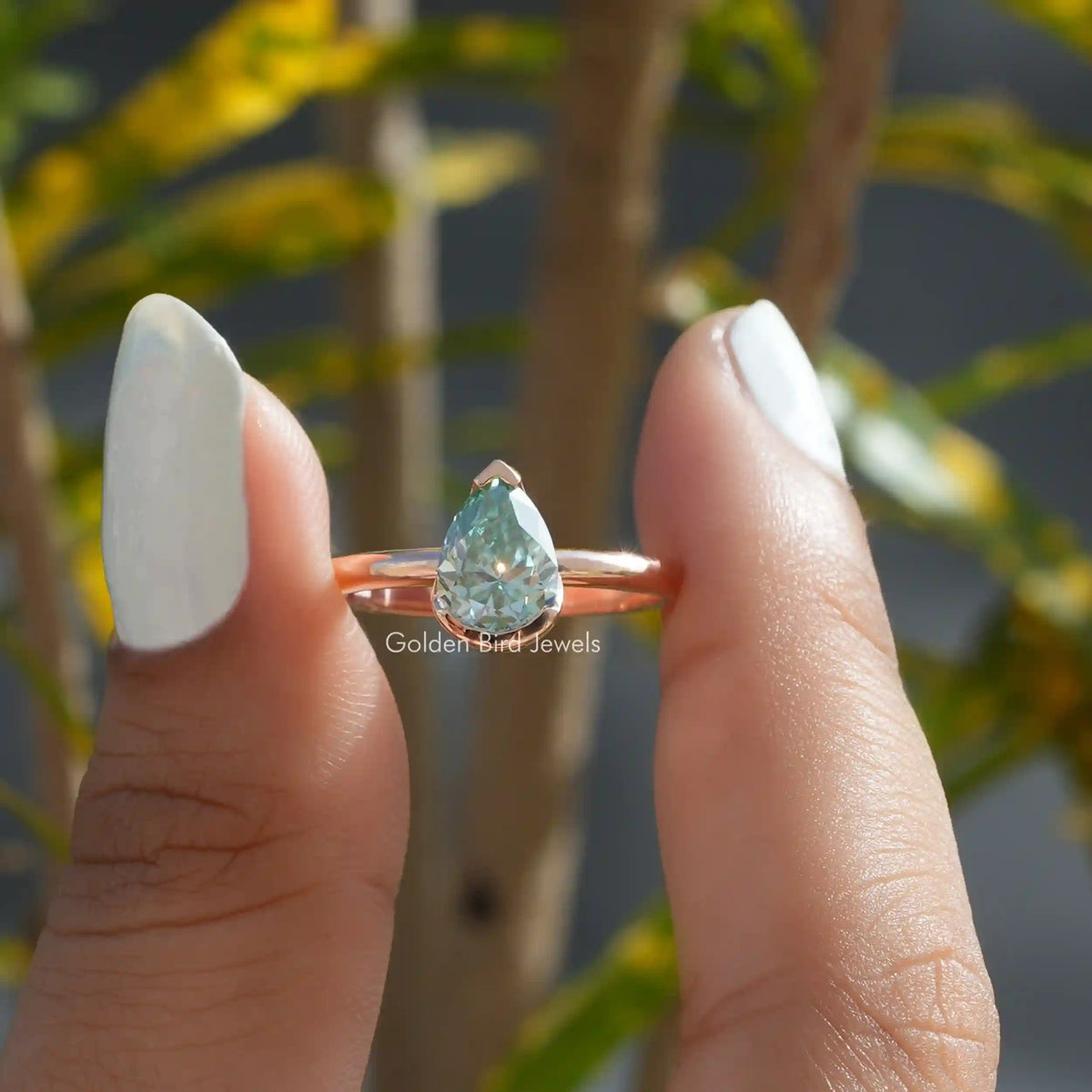 Two fingers holding the Moissanite Pear Cut V Prong Set Solitaire Ring 