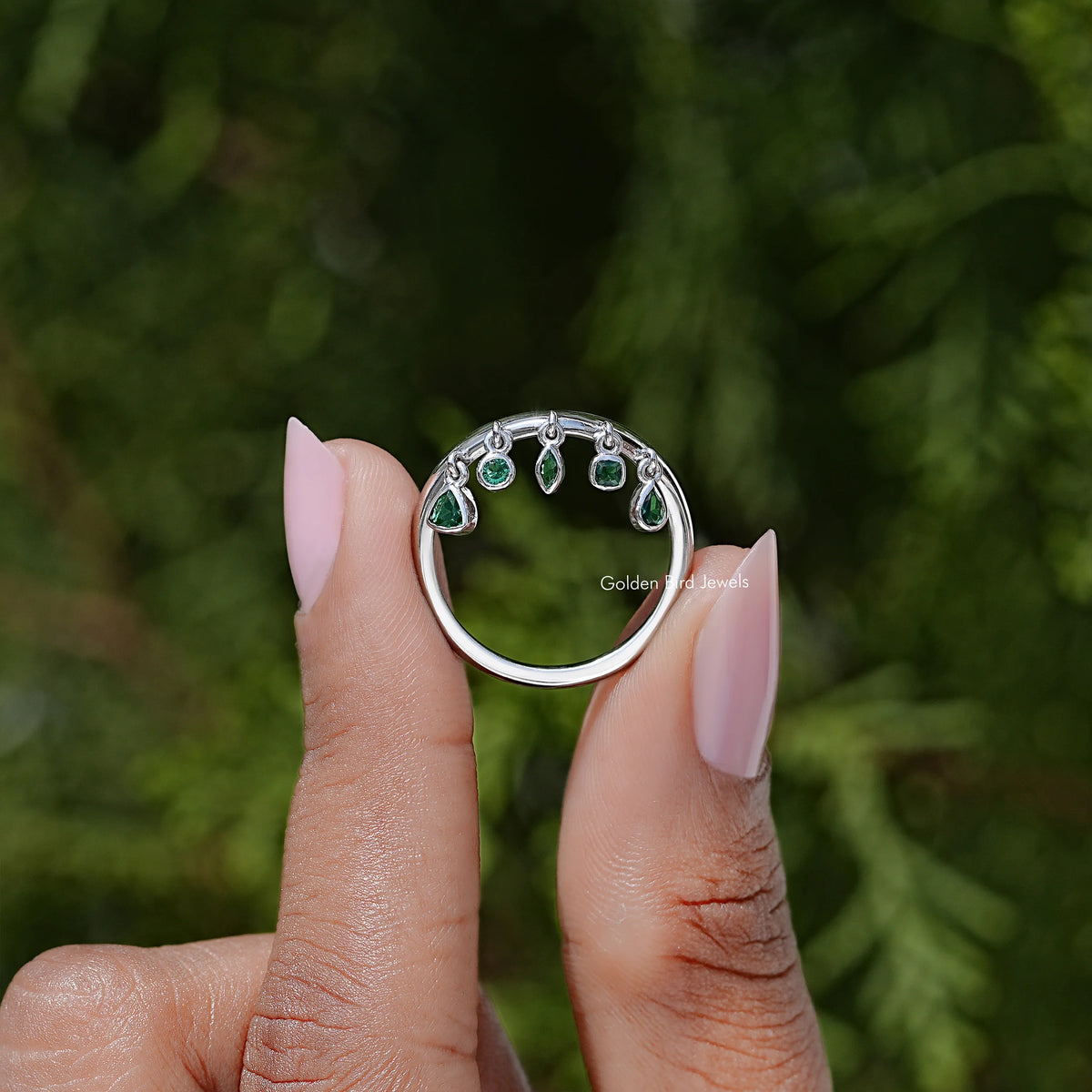 Curved engagement ring with multiple green gemstones in bezel settings, silver