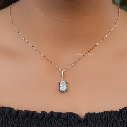 Solitaire pendant necklace worn on a fine chain, with a clear emerald-cut stone and dark setting