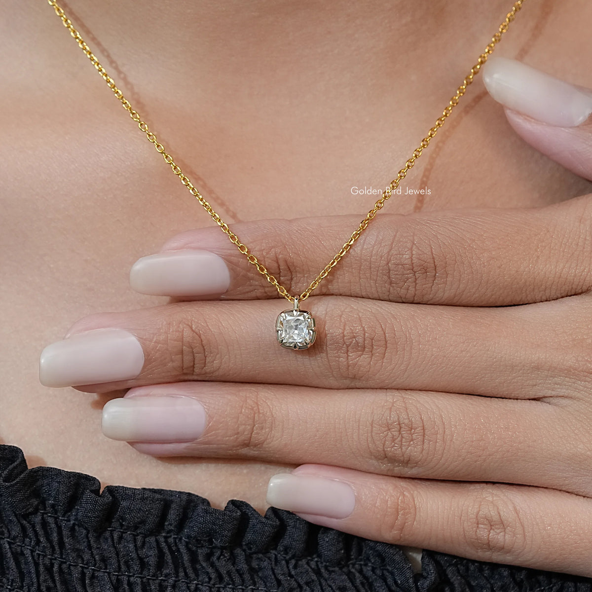 Gold tone moissanite pendant in round prong setting on chain, held in hand