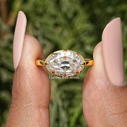 Oval moissanite solitaire ring with gold-tone band, worn on a hand.