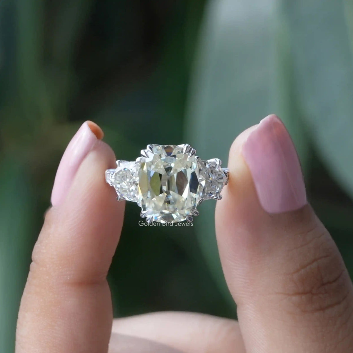 Two fingers holding the Old Mine Cushion Cut Three Stone Moissanite Ring