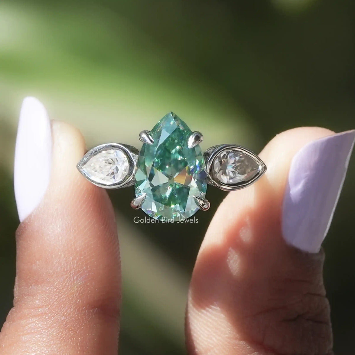 Two fingers holding the Pear Cut Moissanite Three Stone Ring