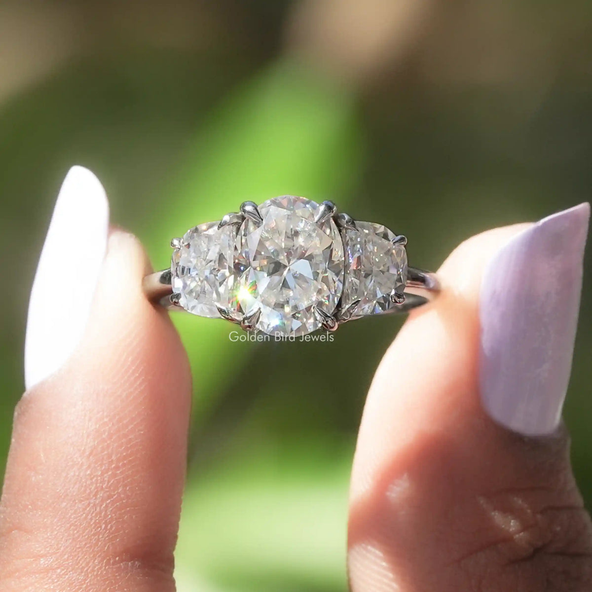 Two fingers holding the Oval And Half Moon Cut Three Stone Moissanite Ring