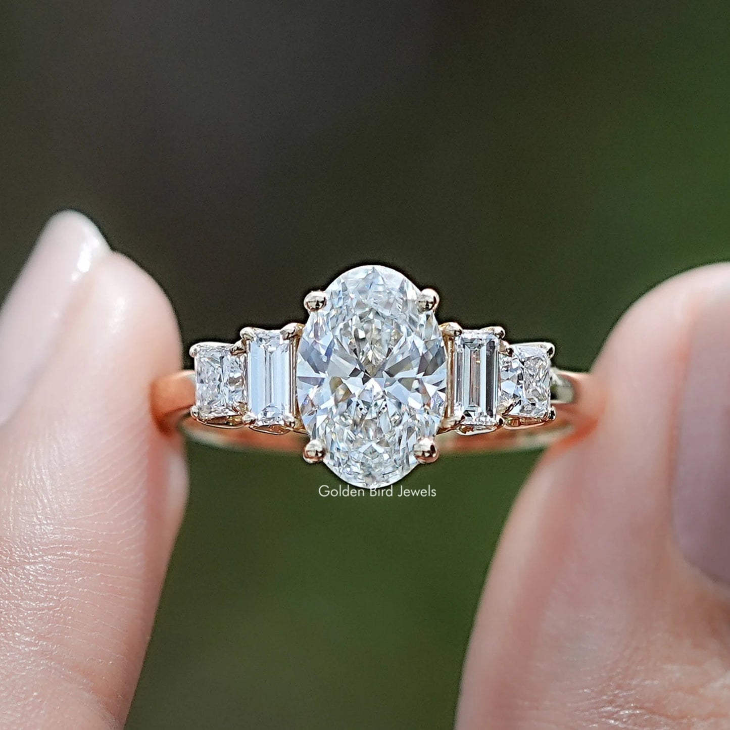 Oval Cut Lab Diamond Five Stone Engagement Ring BetweenTwo Fingers