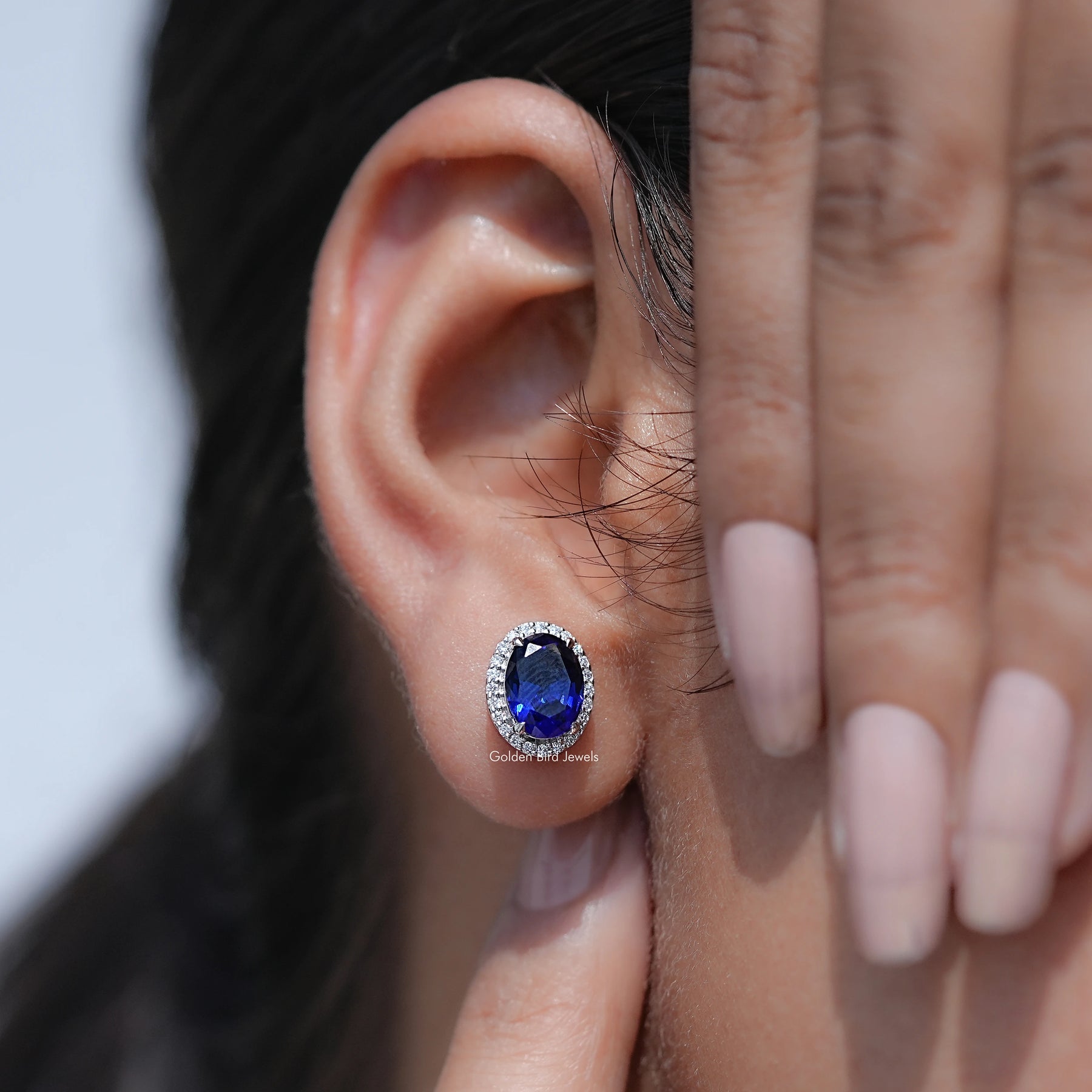 Close-up of an ear wearing a blue gemstone earring with a hand adjusting it