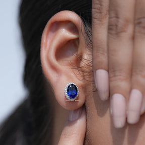 Close-up of an ear wearing a blue gemstone earring with a hand adjusting it