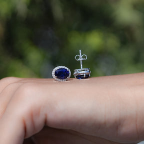 Sapphire earrings on a hand with a blurred green background
