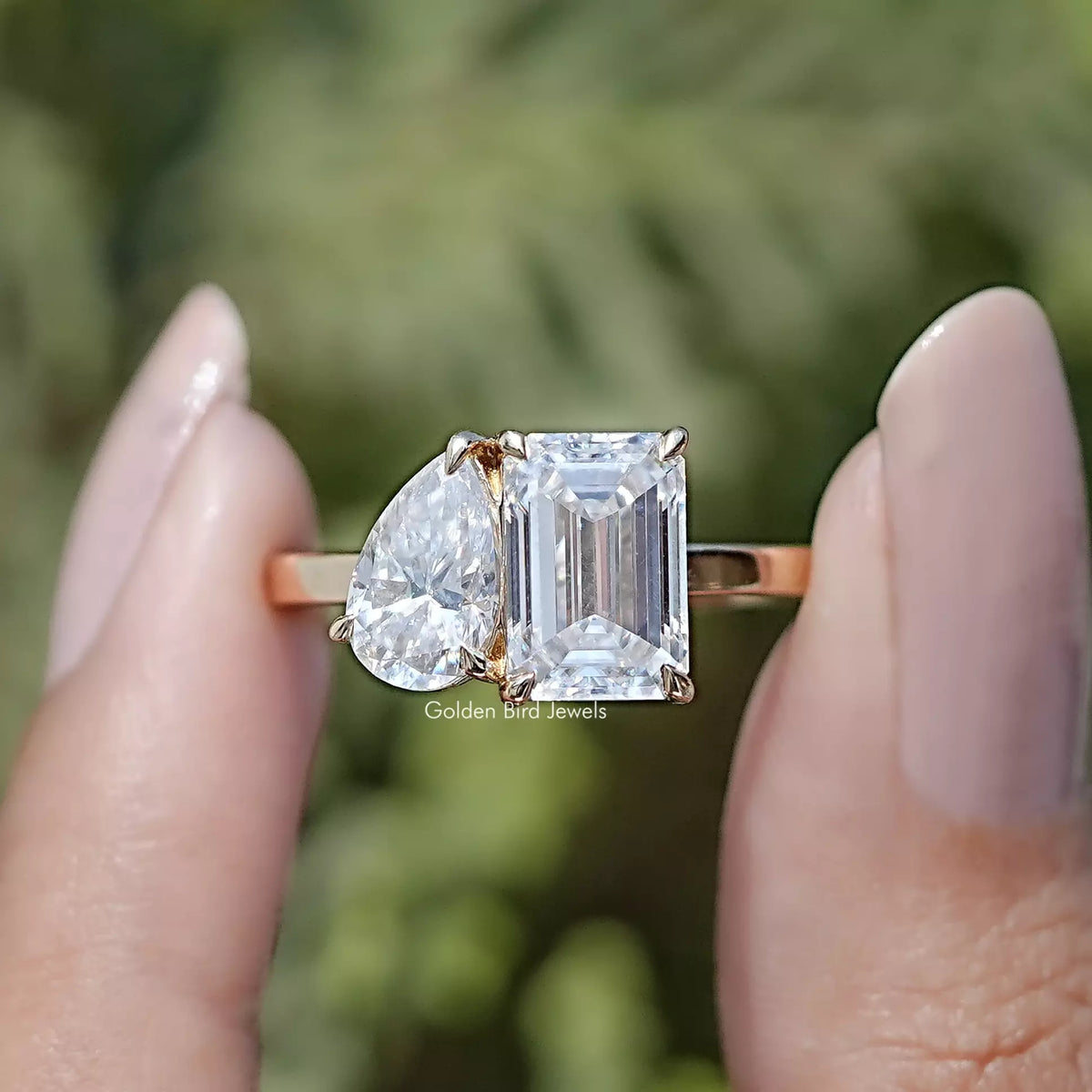 Front view of Pear And Emerald Cut Moissanite Two Stone Ring in two fingers 