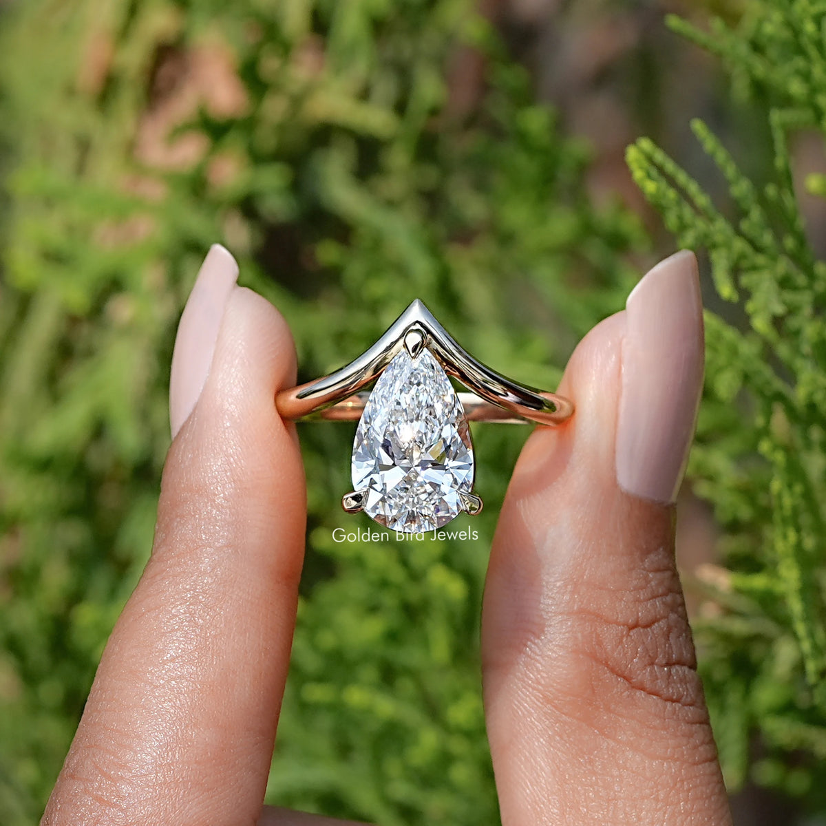 Front View of Pear Cut Curved V Shaped Shank Solitaire Ring In two Fingers