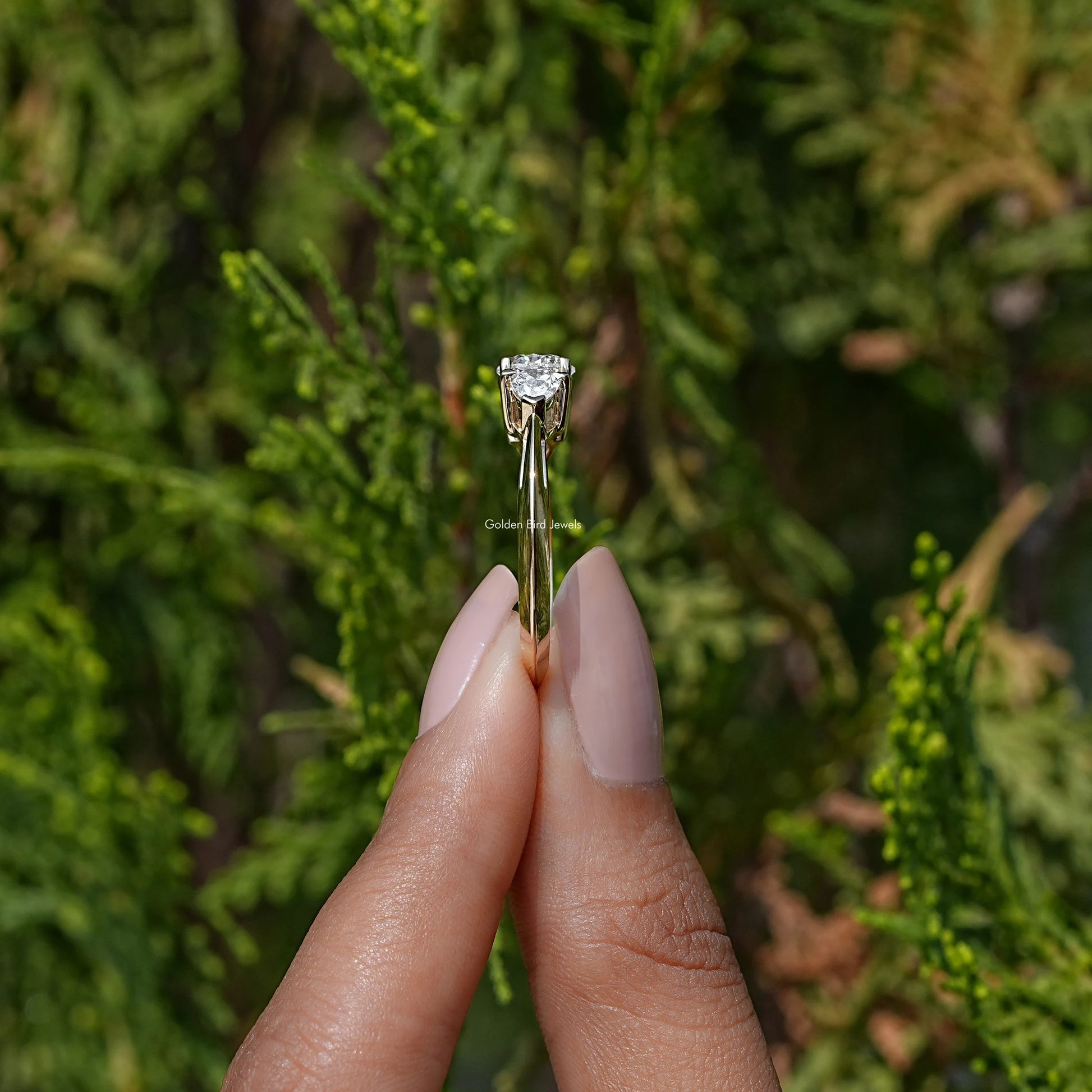 Side View of Pear Cut Lab Diamond Three Stone Engagement Ring In two fingers