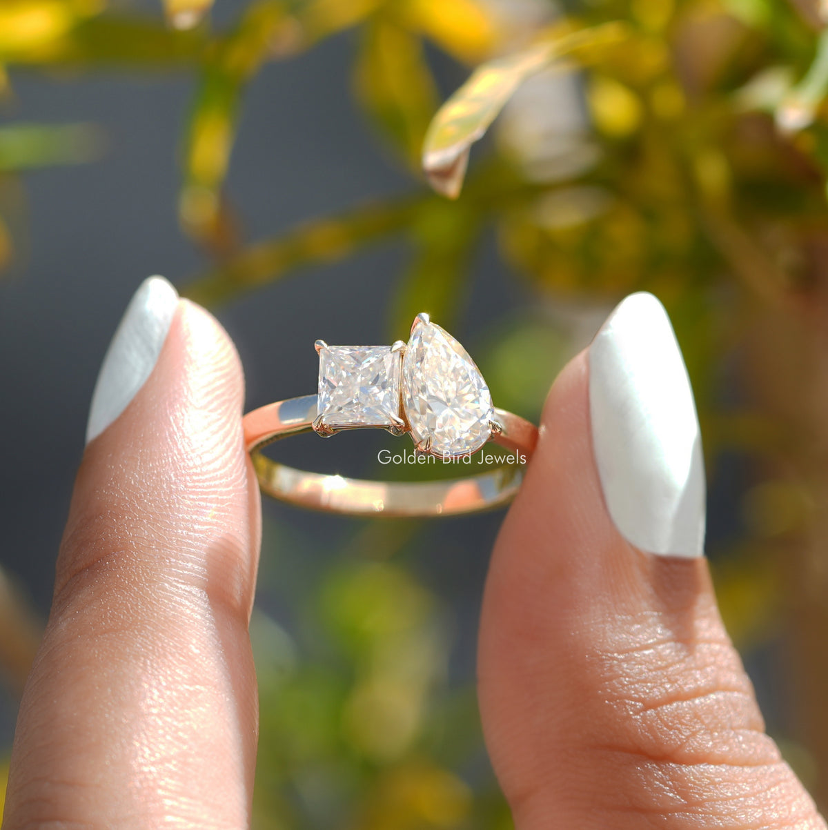 Two fingers holding the Pear And Princess Cut Moissanite Ring 