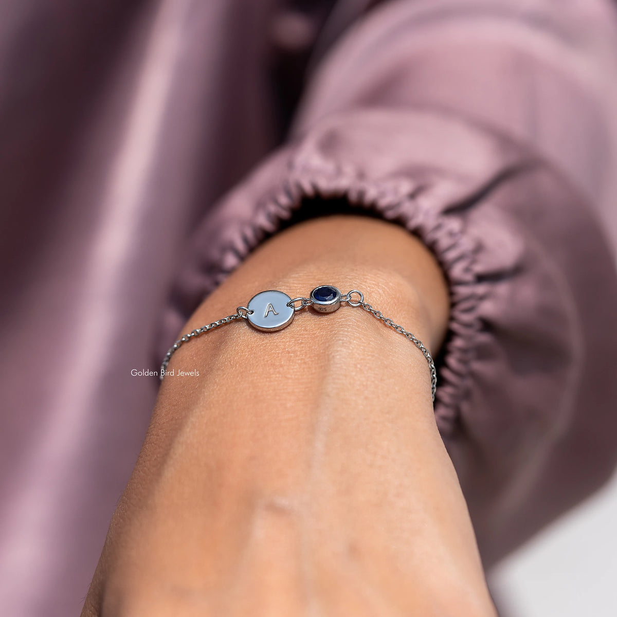 Sterling silver bracelet with A charm and blue round gemstone on forearm