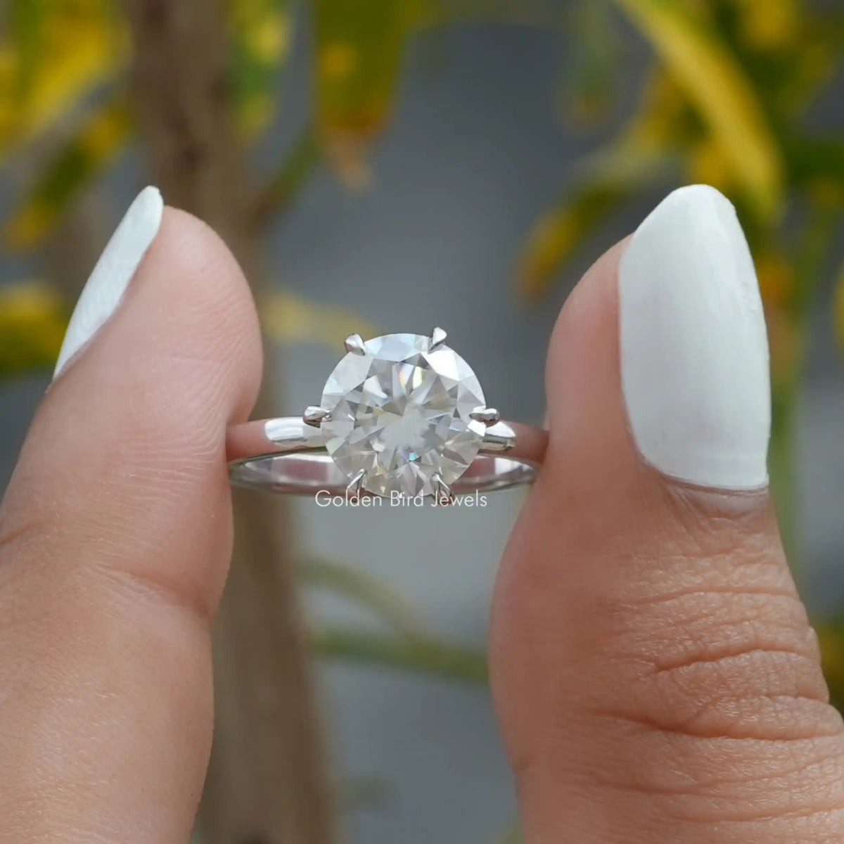 Round Cut Moissanite Engagement Ring held between two fingers
